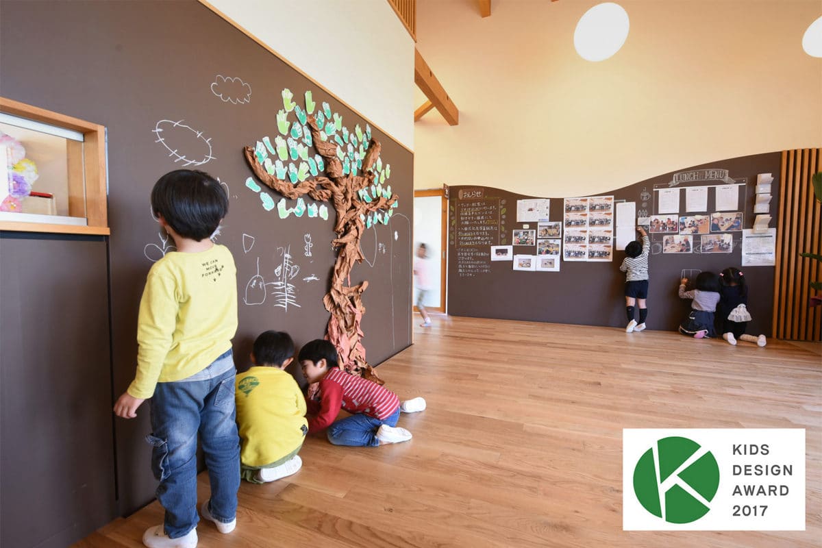黒板塗装の壁に子どもたちが手形の木を作っている園内の様子