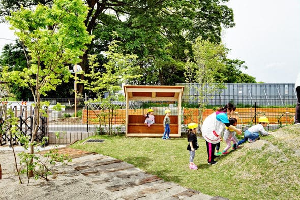 園庭の芝生と木の遊具のまわりで遊ぶ子どもたち