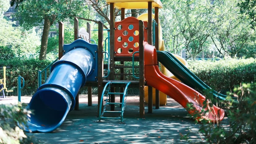 木々に囲まれた園庭に置かれた、すべり台とトンネル遊具のある屋外遊具の写真