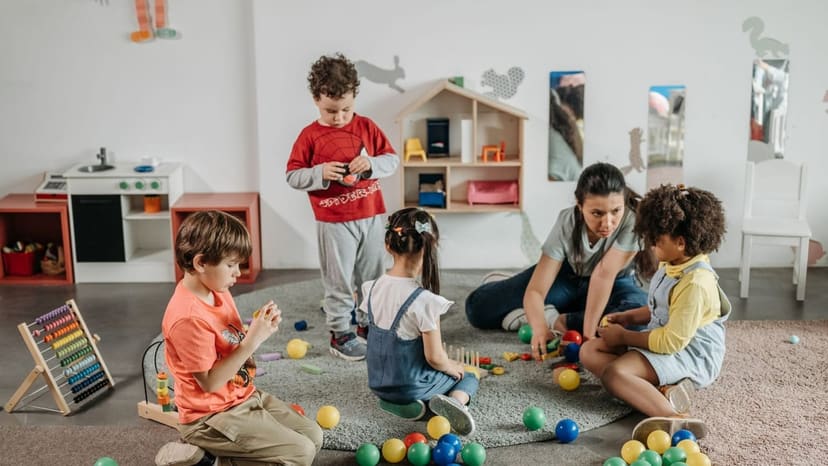 保育室の床で、保育者と子どもたちがボールや積み木で遊んでいる