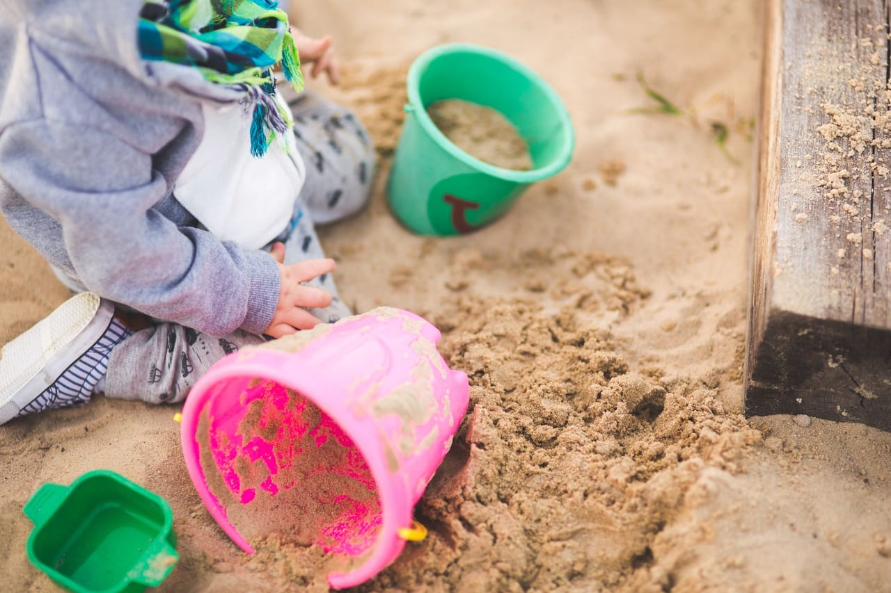 砂場で色とりどりのバケツを使って遊ぶ、子どもの手元を上から見た様子