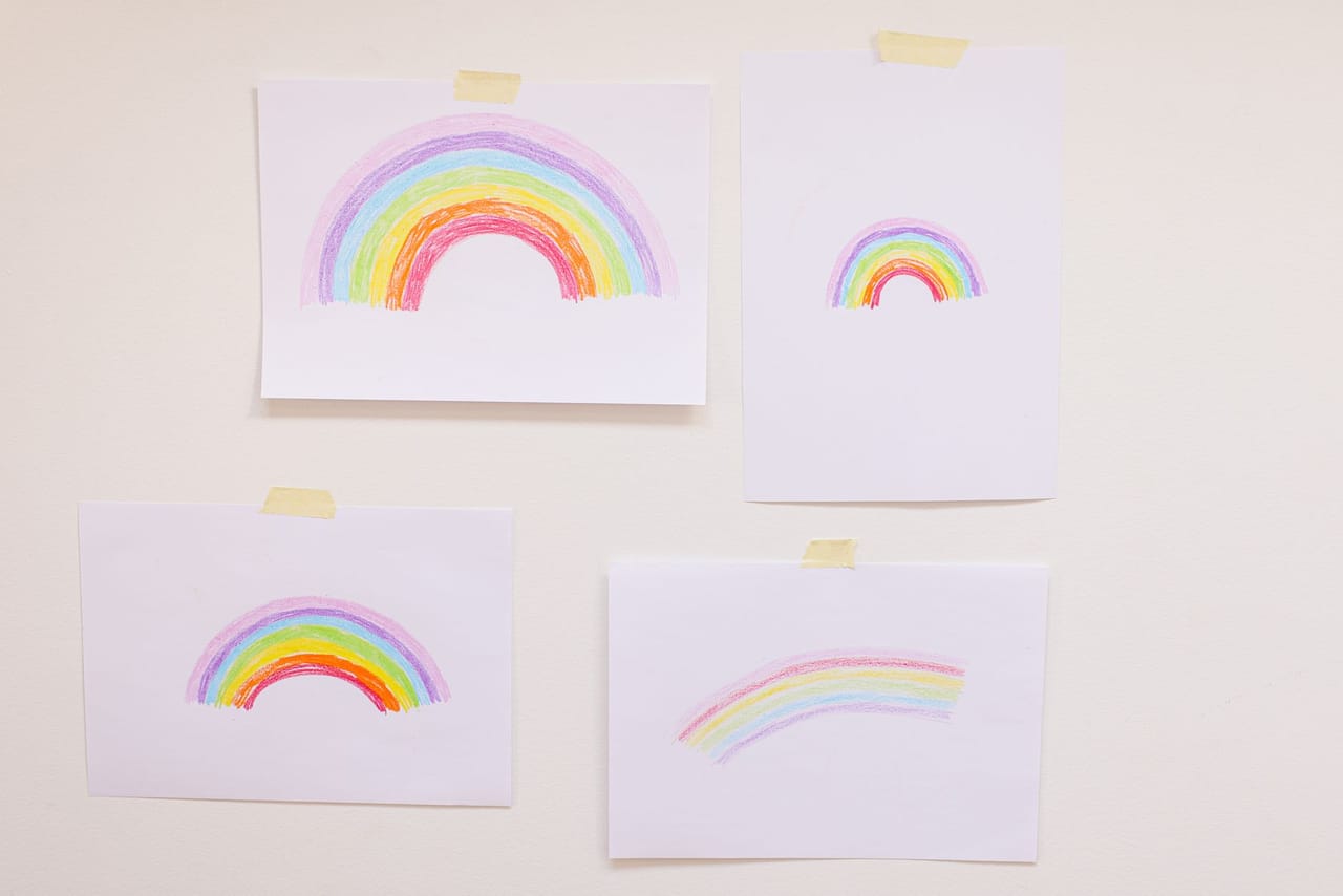 子どもが描いた虹の絵が、低い位置に何枚もテープで壁に貼られている